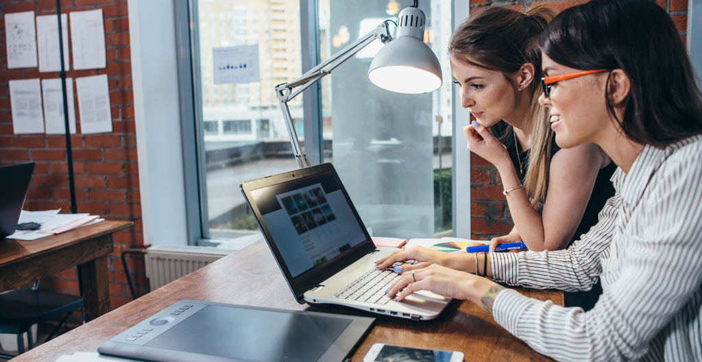 Des mains tapent sur un clavier d'ordinateur portable avec un carnet de notes ouvert à côté, plan serré dans un bureau épuré